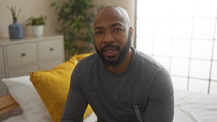Handsome young man sitting in a cozy bedroom with indoor plants and modern decor, looking directly at the camera and smiling
