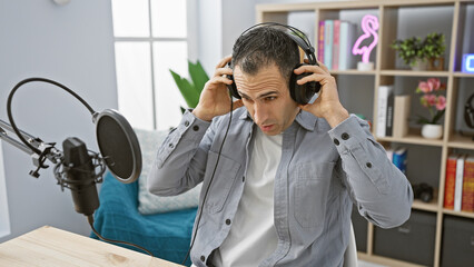 A hispanic man wearing headphones speaks into a microphone in a modern radio studio.