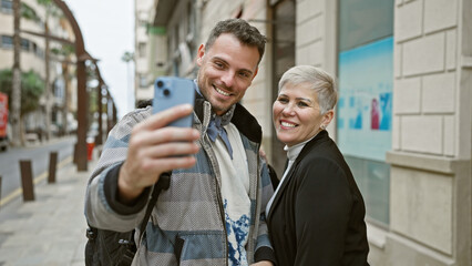 A smiling man and woman taking a selfie together on a city street, capturing a moment of urban connectivity and joy.