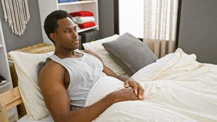 Thoughtful african man sitting in bed at home, contemplating in a bedroom setting.