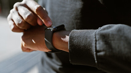 A young black man uses a smartwatch on his wrist in an urban outdoor setting.