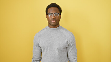 Portrait of a young adult african american man with glasses against an isolated yellow background