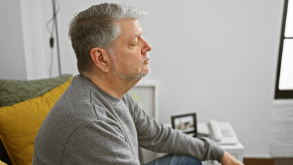 Obraz premium Serene mature man with grey hair in a casual setting at home, embodying tranquility and contemplation.