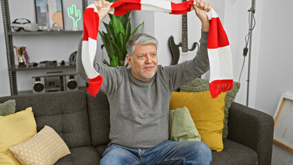 Cheerful middle-aged man celebrating with a red and white scarf in a cozy living room setting