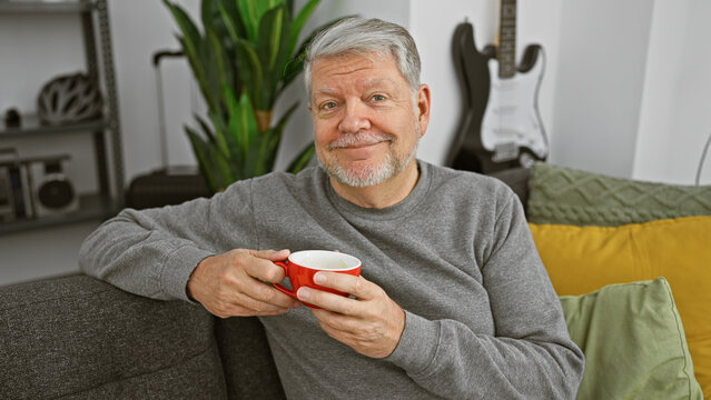 Smiling senior man with grey hair enjoying a cup of coffee in a cozy living room.