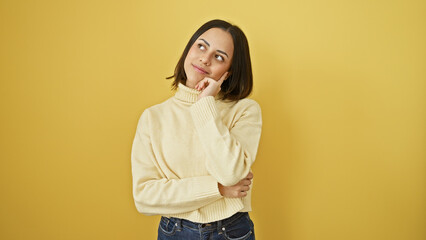 A contemplative young hispanic woman in a white sweater against a yellow background, portraying a...