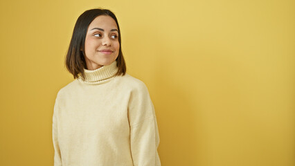 Fototapeta premium Portrait of a young hispanic woman in a white sweater against a yellow background, conveying a sense of beauty and elegance.