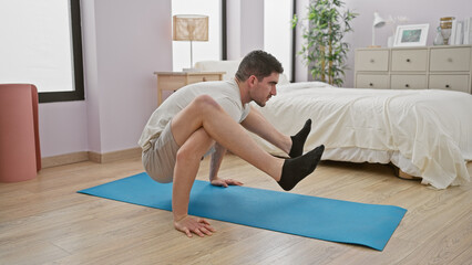 Young man exercises on a blue yoga mat in a modern bedroom, displaying fitness and healthy lifestyle at home.