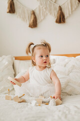 Cute beautiful girl baby sitting on the bed in the bedroom and playing in eco wooden toys cubes and pyramid