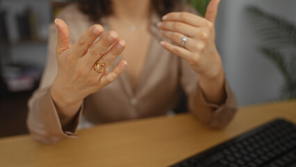 A hispanic woman gesturing with her hands in an office setting, emphasizing her rings, against a background of indoor office decor.