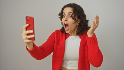 A young hispanic woman holds a red phone, expressing surprise with wide eyes and an open mouth...