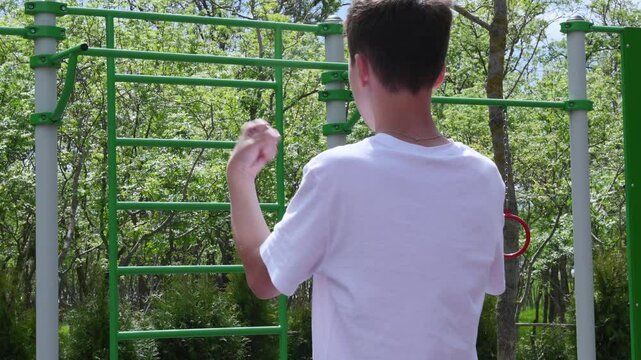 thin teenager, a schoolboy of 14 years old, plays sports on the playground, pulls himself up, does a warm-up. High quality 4k footage