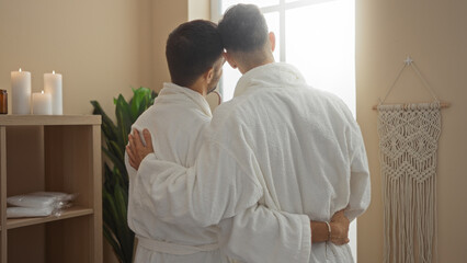 Men couple in white robes embracing while standing in a serene spa room lit with candles, emphasizing love and relaxation in a wellness setting