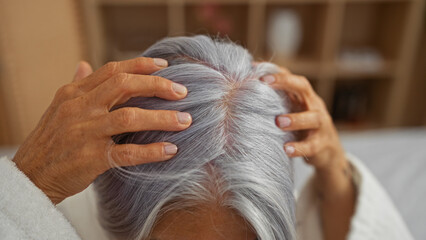 Woman enjoying relaxing head massage in serene spa setting with soft natural light highlighting her mature, silver hair and calm, soothing atmosphere of the wellness center