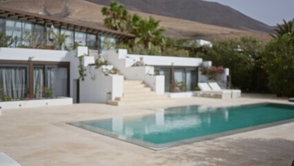 Defocused view of a tropical resort highlighting a pool and sun loungers against a backdrop of greenery and distant mountains