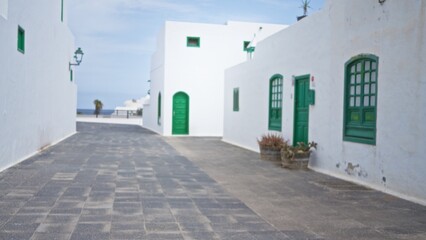 Blurred street view with white buildings and green doors and windows in an outdoor setting in lanzarote, canary islands, spain with defocused background and bokeh effect.