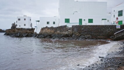 Blurred white houses by the rocky seaside in lanzarote, canary islands, on an overcast day, conveying a serene coastal scene in spain.