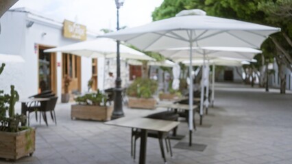 Blurred view of outdoor cafÃ© with umbrellas in lanzarote, spain, showcasing defocused tables and green plants on a sunny day.
