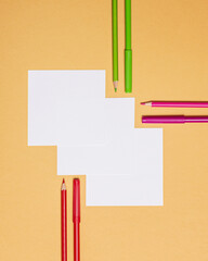 three square sheets of paper with pens and pencils on orange background