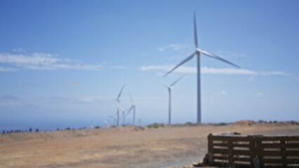 Defocused landscape showcasing large wind turbines used for green electricity generation under a clear blue sky