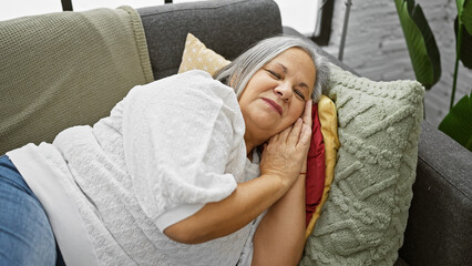 A serene elderly woman rests on a couch, eyes closed, exuding tranquility in a home setting.