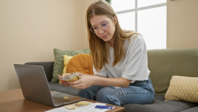 Adult woman counting norwegian kroner at home on couch with laptop.