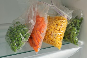 Plastic bags with different frozen vegetables in refrigerator, closeup