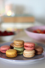 Plate of pastel macarons, cookies and chocolate, cup of tea of coffee, glass of bubble water, various berries, books and accessories on the table. Selective focus, pastel colors.