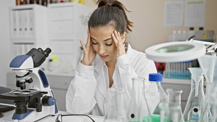 Stressed young woman scientist in lab with microscope and research equipment showcasing healthcare...