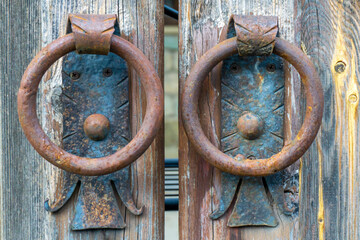 Two rusty donut-shaped knockers rivet onto a wooden door. The wood grain is visible