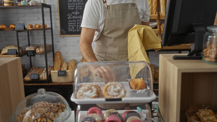 Baker working in a bakery shop arranging pastries and bread, hispanic male hands seen behind the counter in an indoor setting