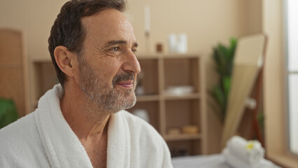 Middle-aged hispanic man enjoying a relaxing moment at a spa wears a white robe in a serene...