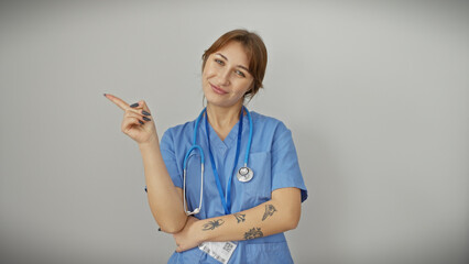 Confident young female nurse in blue scrubs pointing aside against an isolated white background.