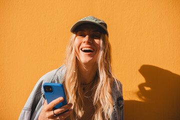 Happy laughing blonde curly woman read sms, good news, joke and smiling standing isolated on yellow...