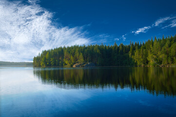 Fototapeta premium Lake in Sweden with white clouds, blue water and trees on the shore. Scandinavian