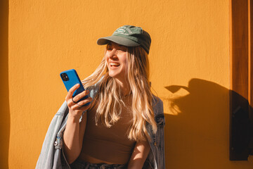 Happy laughing blonde curly woman read sms, good news, joke and smiling standing isolated on yellow...