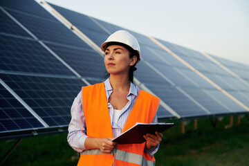 Checking the data, with notepad. Female worker engineer in uniform is near solar panels