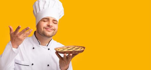 Smiling Baker Guy Smelling Baked Pie Standing Over Yellow Background. Culinary Recipes Concept. Studio Shot