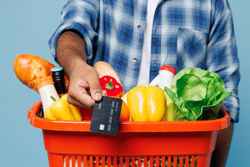 Close up cropped young man wear shirt hold red basket with food products vegetables show mock up of...