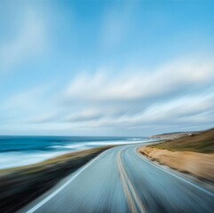 Fototapeta premium Carretera vacía junto al océano con efecto de movimiento, capturada en un paisaje costero, bajo un cielo azul con nubes dispersas.