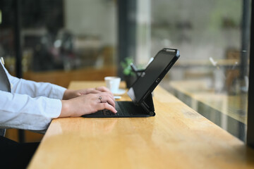Cropped shot of female freelancer typing on wireless keyboard of digital tablet, working at cafe