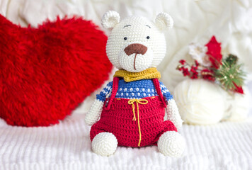 Knitted polar bear amigurumi toy in knitted clothes on white background with Christmas decorations, handmade toys