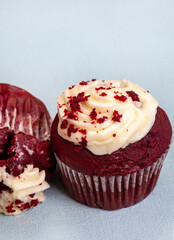 Two red velvet cupcakes, one upside down squashed one. Light pastel blue background