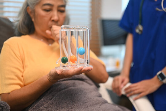 Mature woman using a spirometer to help patients to improve the functioning of lungs under healthcare professional