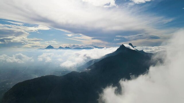 Aerial ascend of Toix Mountain in Calpe, Spain, with clouds surrounding the peaks. The mountain rises dramatically from the misty valley below.