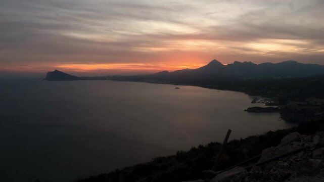 Timelapse of the sun setting over the Mediterranean Sea from Toix Mountain in Calpe, Spain. Clouds roll through as light fades.