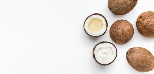 Whole coconuts, coco oil and water in halves of coconut on white background top view, copy space. Magic nut concept