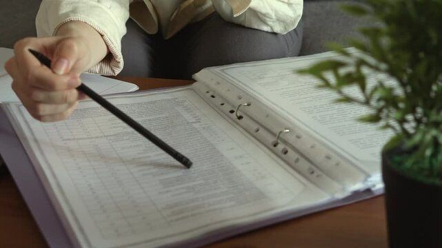 The girl looks for the necessary data in the documents and points to them with a pencil. Working from home with documents. Digitization 