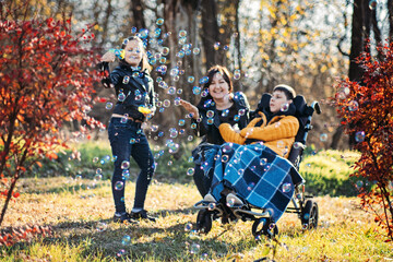 Mother and sibling spending quality time with child in wheelchair, outdoor play with bubbles,...