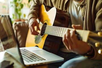 Fototapeta premium A person strumming a guitar next to a laptop, creative workspace setup